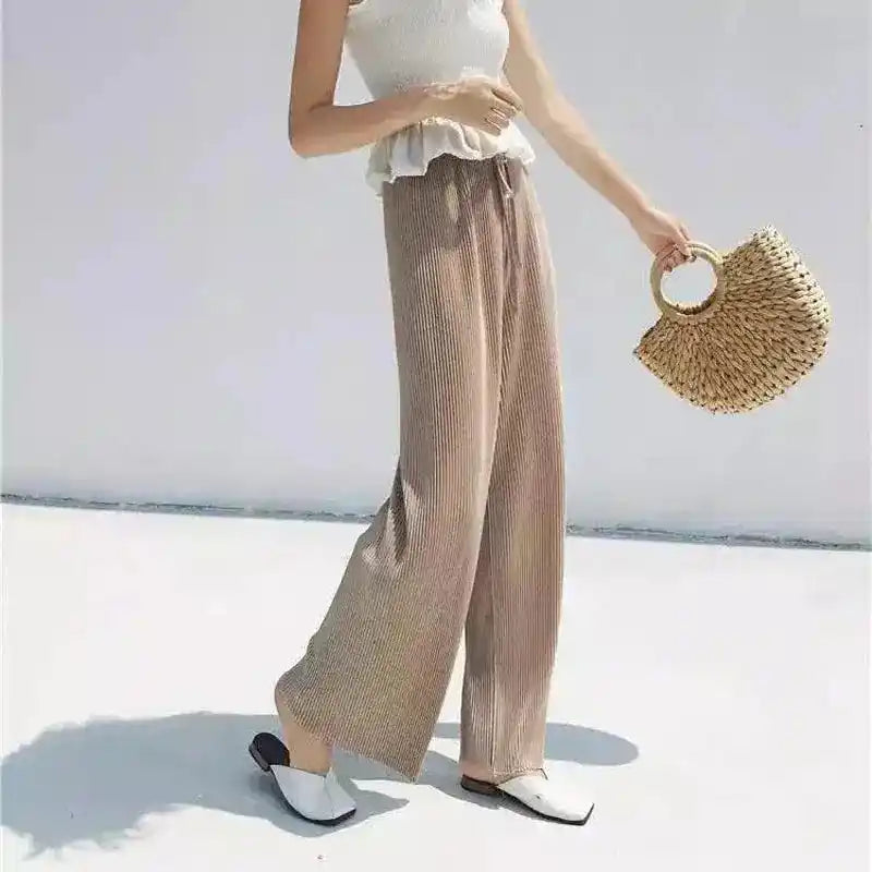 Person wearing beige wide-leg pants and a white top, holding a straw bag on a light background