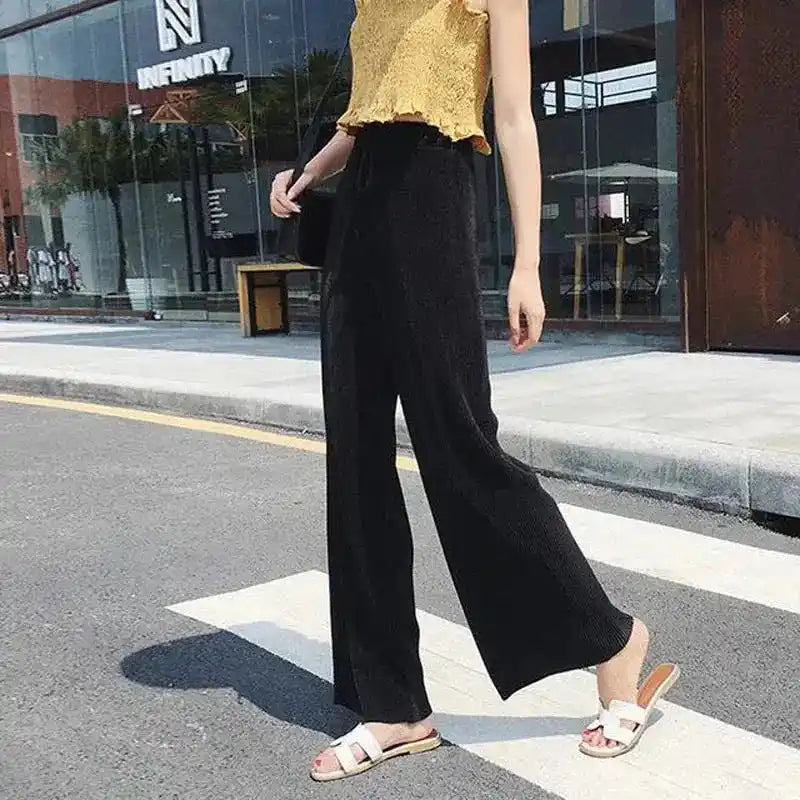 Person wearing black wide-leg pants and a gold top on a city street.