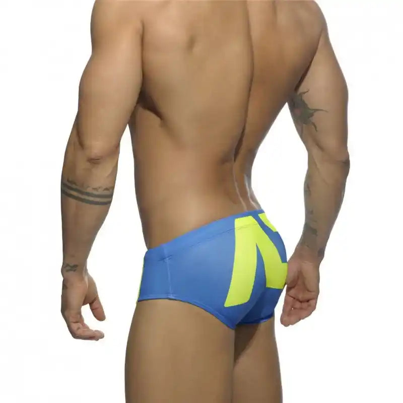 Rear view of men's low-waist swim briefs in blue and neon yellow, featuring a sporty and vibrant summer look.