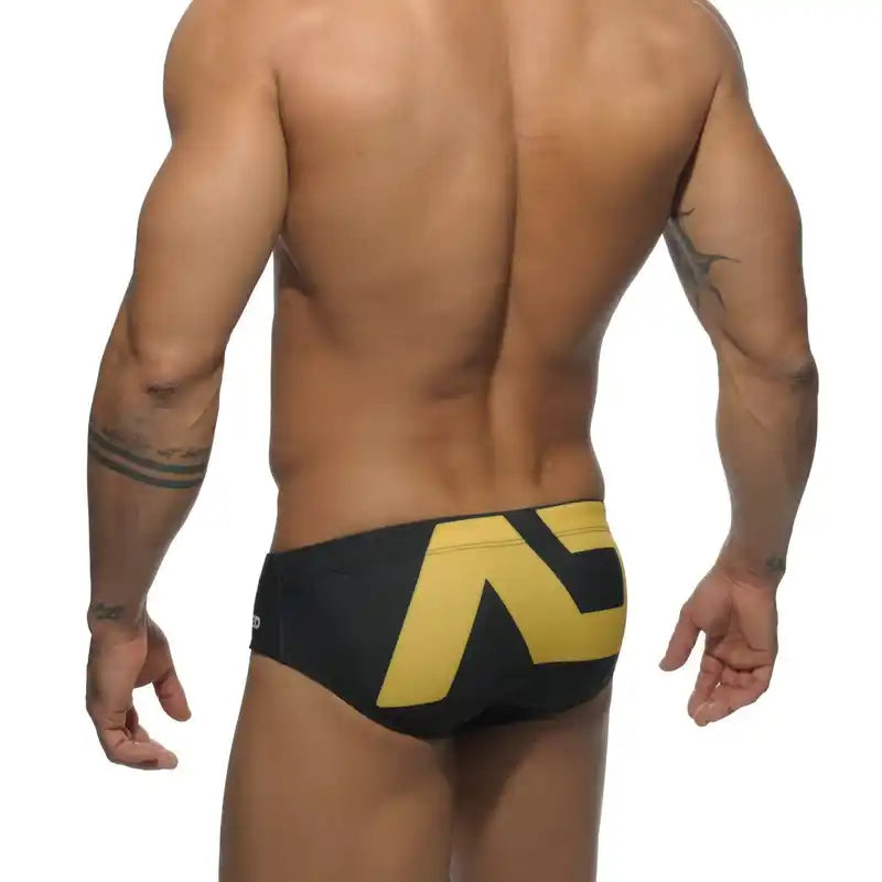 Back view of men's low-waist swim briefs in black and yellow, showcasing a snug fit and bold geometric print.