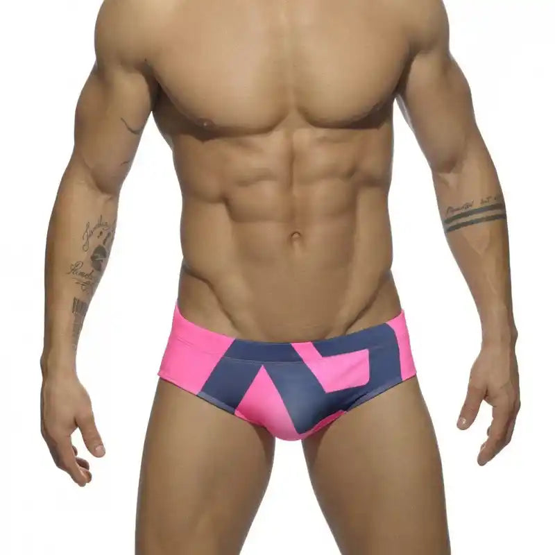 Men's low-waist swim briefs in pink and navy with angular design, combining bold color with a streamlined fit.